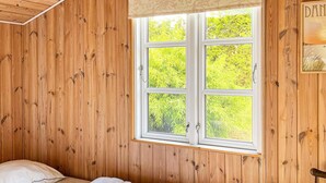 A wooden-paneled room with a bed, a window, and a door. - Holiday Home in Hadsund (Hadsund)