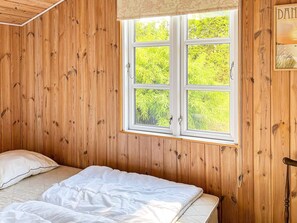 A wooden-paneled room with a bed, a window, and a door. - Holiday Home in Hadsund (Hadsund)