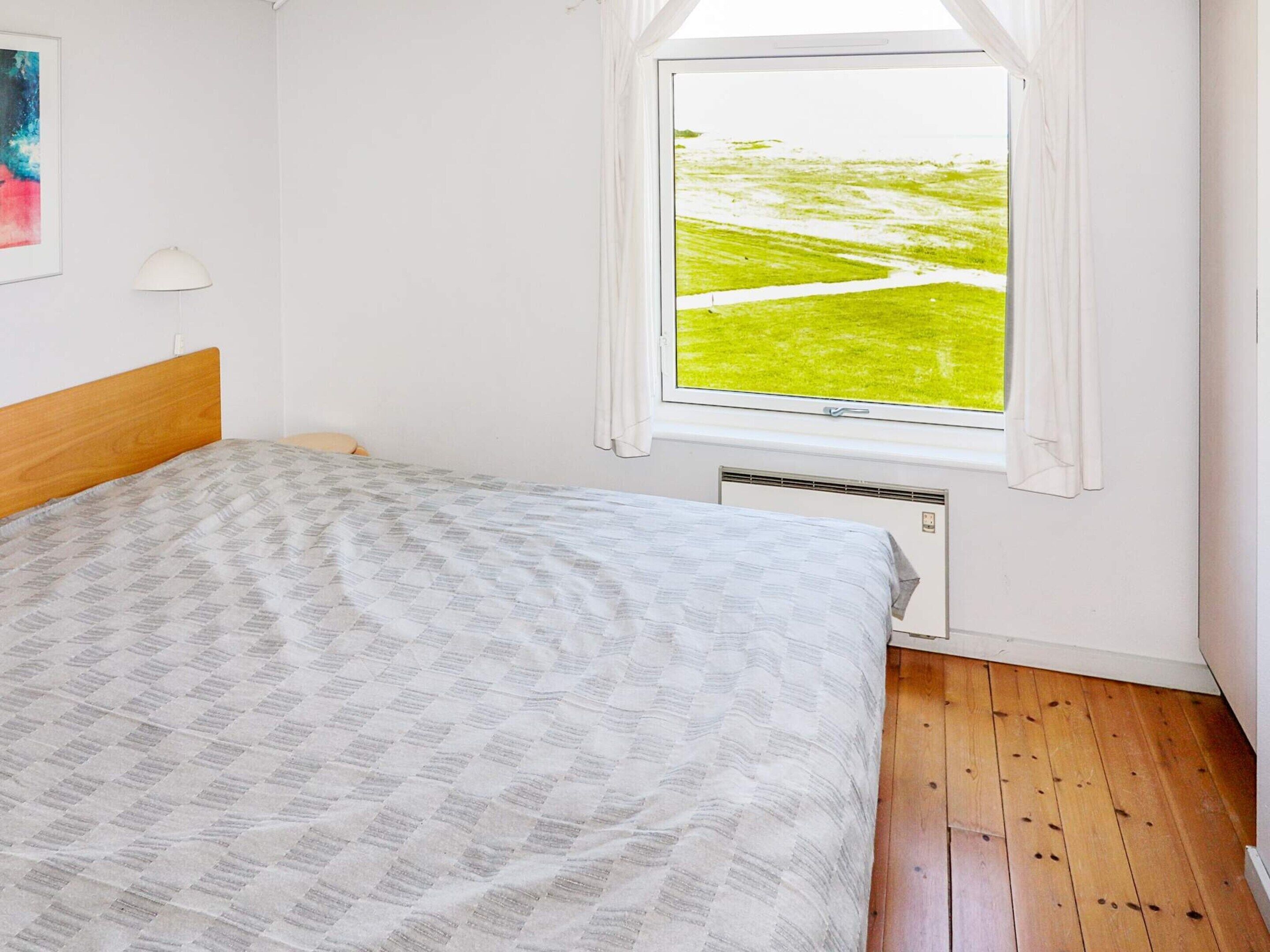 Un dormitorio con cama, ventana con vista a un paisaje verde y una lámpara de pared.