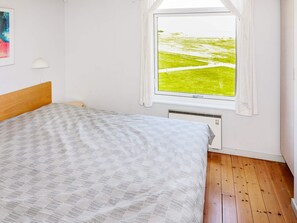 A bedroom with a bed, a window with a view of a green landscape, and a wall-mounted lamp.