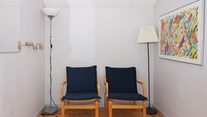 A room with two wooden chairs with dark blue cushions, a white floor lamp, and a colorful abstract painting on the wall.