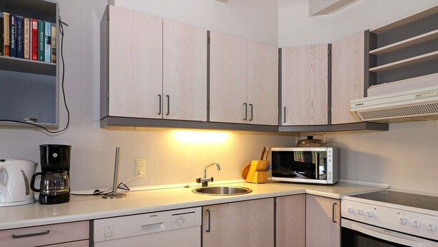 A modern kitchen with light wood cabinets, a built-in microwave, a coffee maker, and a dishwasher.