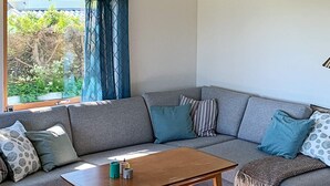 Uma sala de estar moderna com um sofá modular cinza, uma mesa de centro de madeira e vista para o verde lá fora.