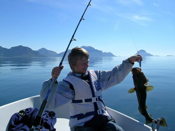 Una persona en un bote sosteniendo un pez, con un lago tranquilo y montañas al fondo.