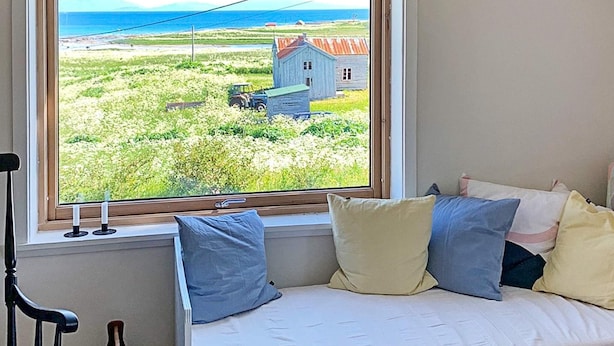 Quarto com janela que oferece vista para um campo gramado e uma casa pequena.