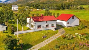 Paisagem rural com uma casa branca e telhado vermelho, cercada por campos verdes e árvores.