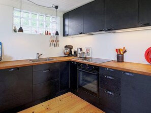 A modern kitchen with dark cabinetry, a wooden countertop, a built-in oven, and a window with a view of greenery. - 5 Person Holiday Home in Jaegerspris (Jægerspris)