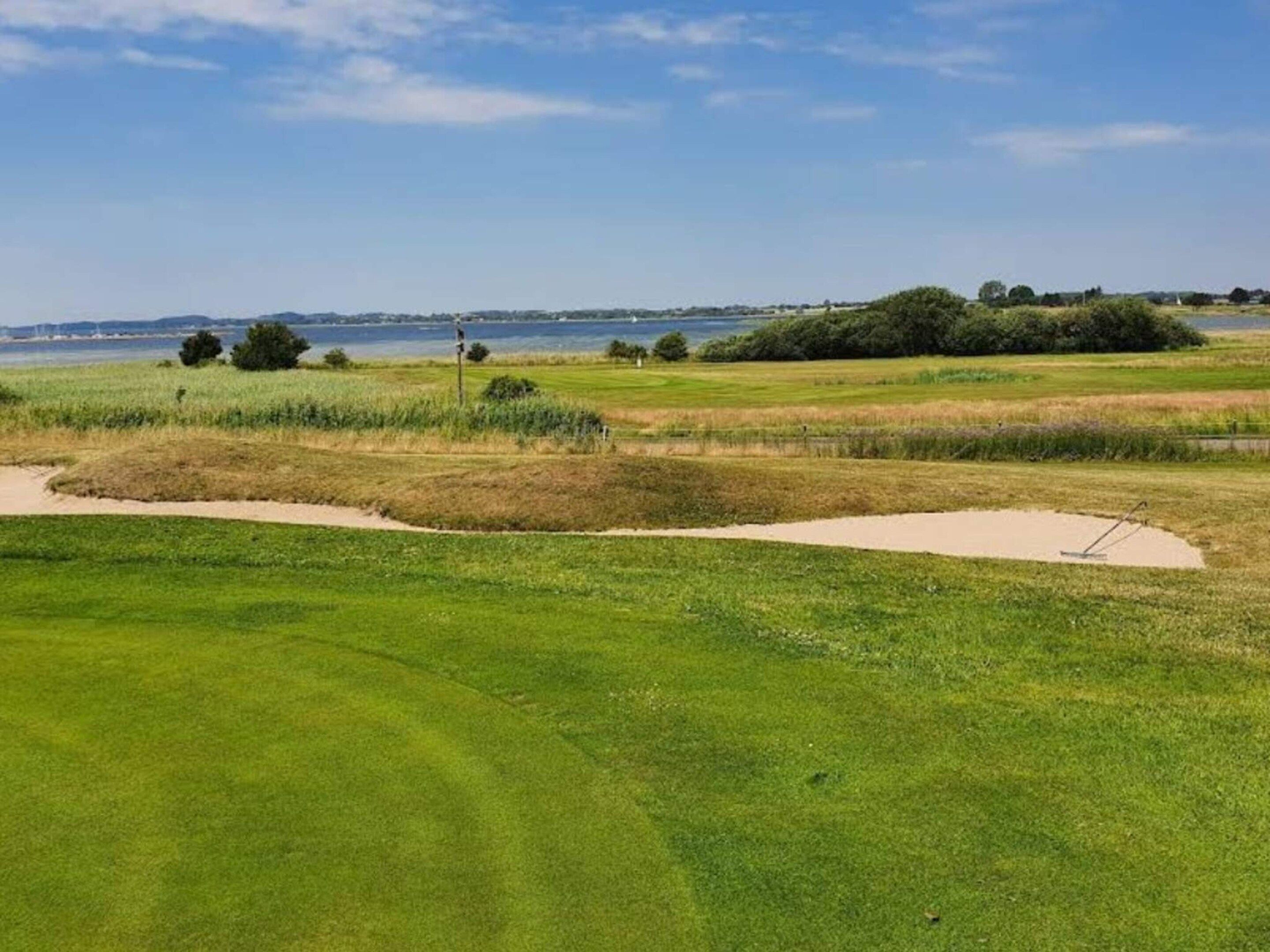 En golfbane med sandbunker, peg og udsigt til vand i baggrunden.