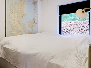 Una habitación con una cama, un mapa en la pared y una ventana con vistas a una pila de troncos.