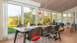 Een ruime eethoek met een moderne tafel en stoelen, grote ramen met uitzicht op de omgeving, en een houten plafond.