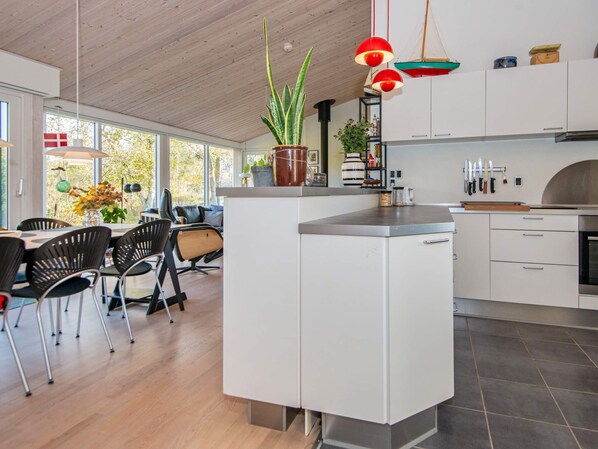 Une cuisine moderne avec des meubles blancs, un îlot central et un coin repas doté de chaises noires.