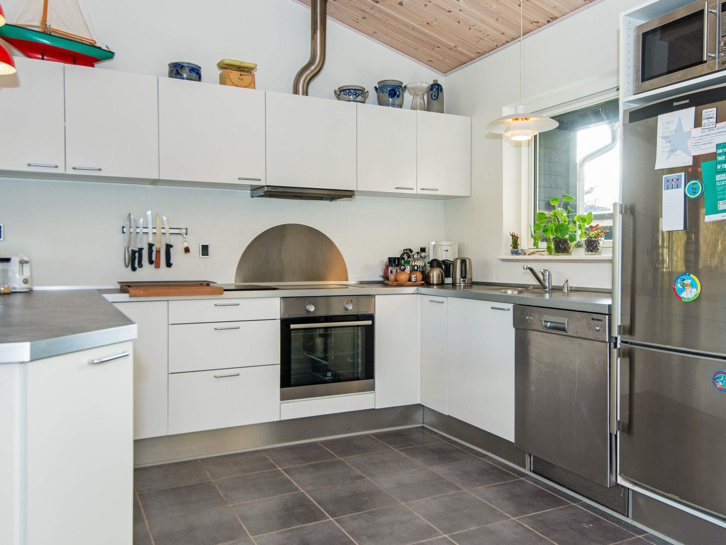 Una cocina moderna con armarios blancos, electrodomésticos de acero inoxidable y un ventanal con plantas.