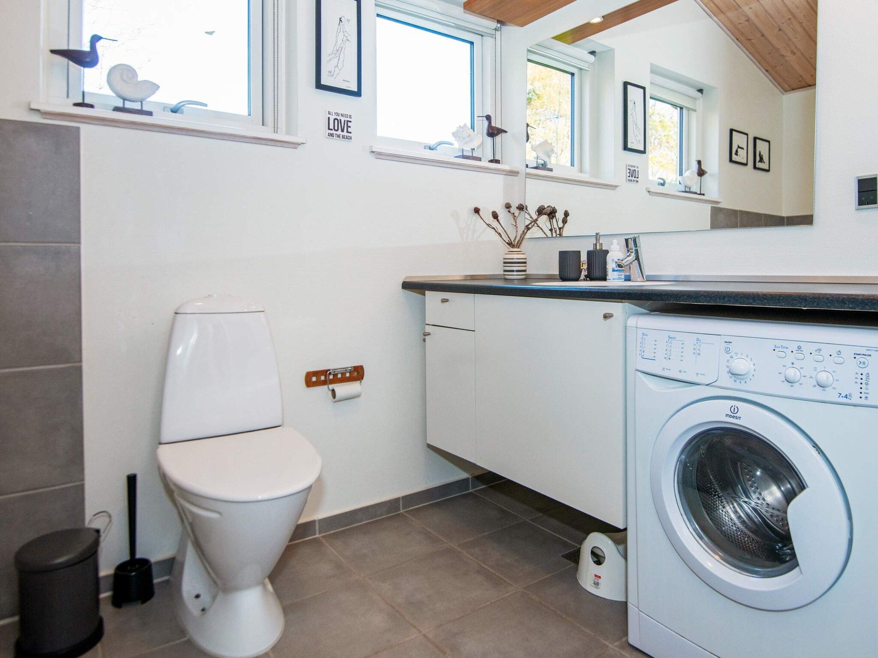 Un bagno compatto con il water, una lavatrice e una finestra decorata.