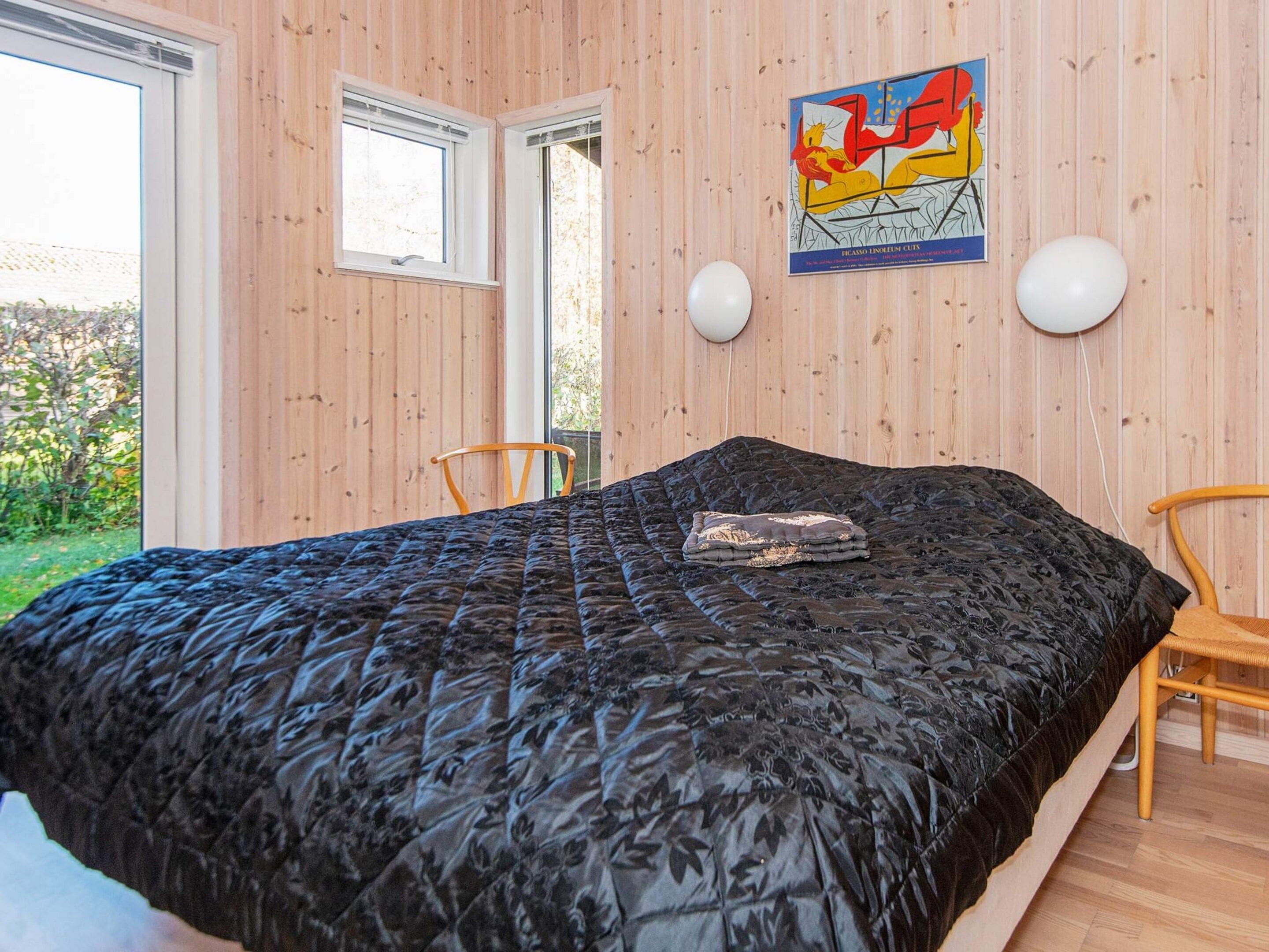 A bedroom with a large bed, two chairs, a window, and a wall-mounted artwork.