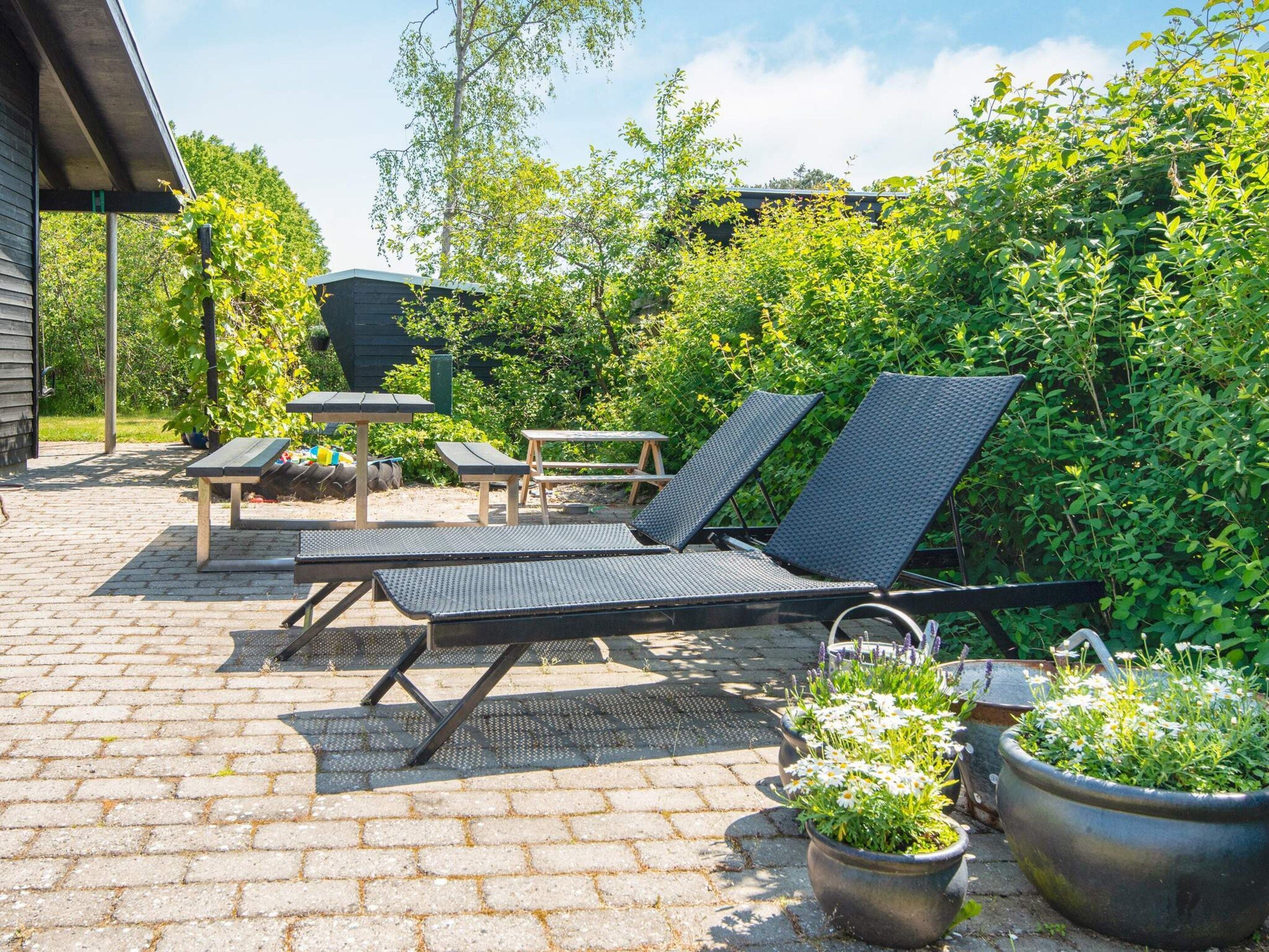 Eine Terrasse mit Liegestühlen, einem Tisch und Pflanzen in Töpfen.