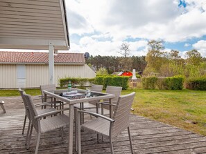 Een houten terras met rieten meubels en een glazen tafel.