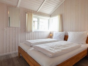 A bedroom with two beds, wooden walls, a window with curtains, and a bedside lamp.