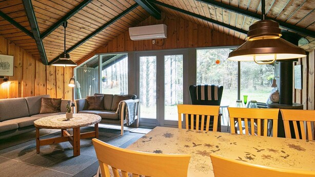 A cozy cabin interior with a wooden ceiling, a sofa, a round table, and a dining table with chairs. - 6 Person Holiday Home in Lokken (Lokken)