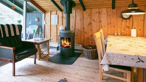 A cozy room with a wood-burning stove, a dining table with a floral tablecloth, and a chair with a striped cushion. - 6 Person Holiday Home in Lokken (Lokken)