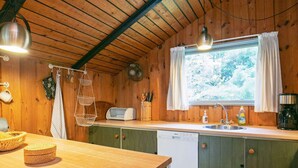 A wooden cabin kitchen with a wooden countertop, a built-in dishwasher, a window with curtains, and hanging kitchen utensils. - 6 Person Holiday Home in Lokken (Lokken)