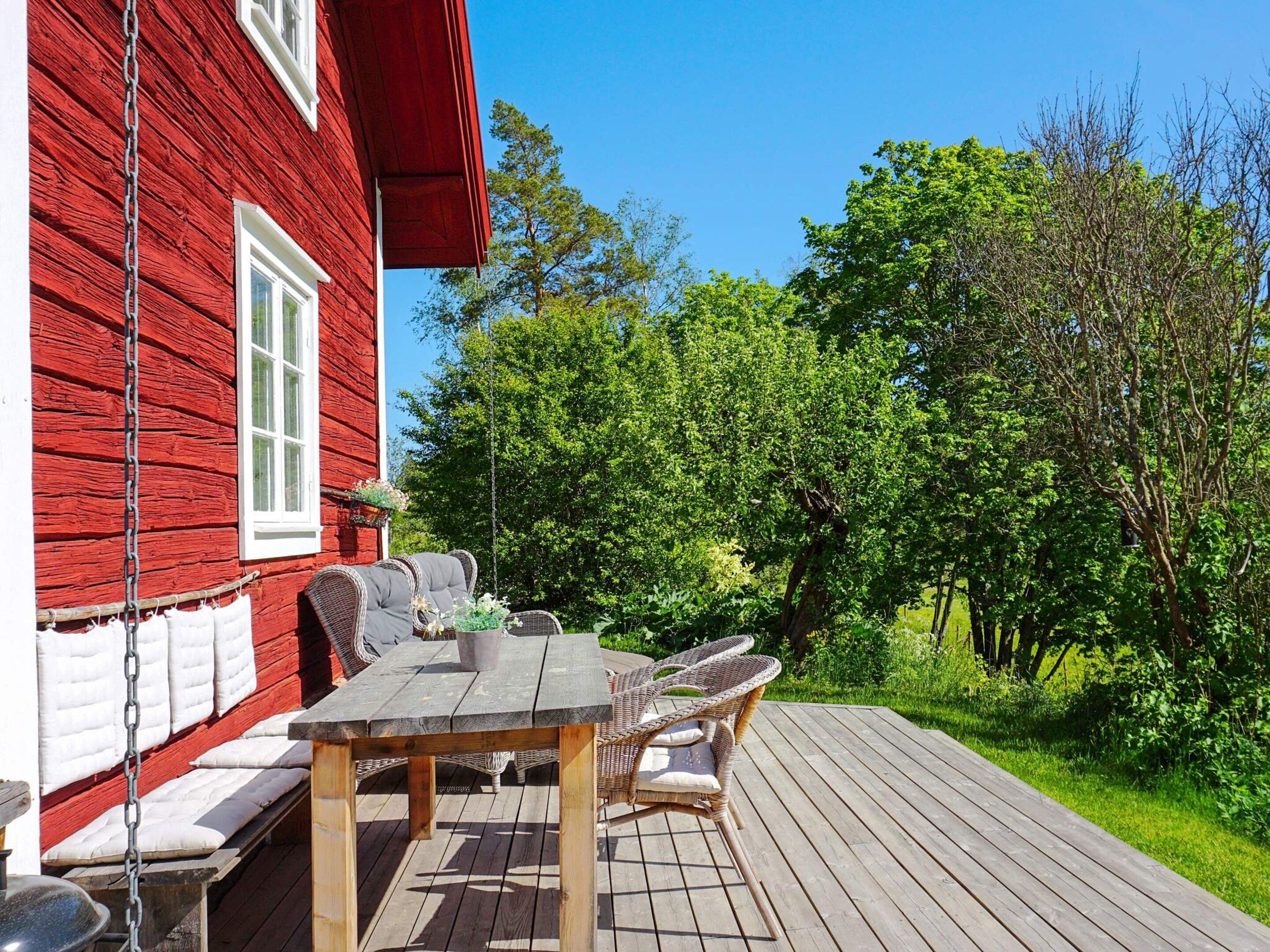 A red wooden house with a deck, wicker furniture, and a hanging chair.