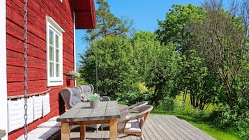 A red wooden house with a deck, wicker furniture, and a hanging chair.