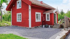 Ein rotes Holzhaus mit geneigtem Dach, einer Veranda und einer Schotterauffahrt.