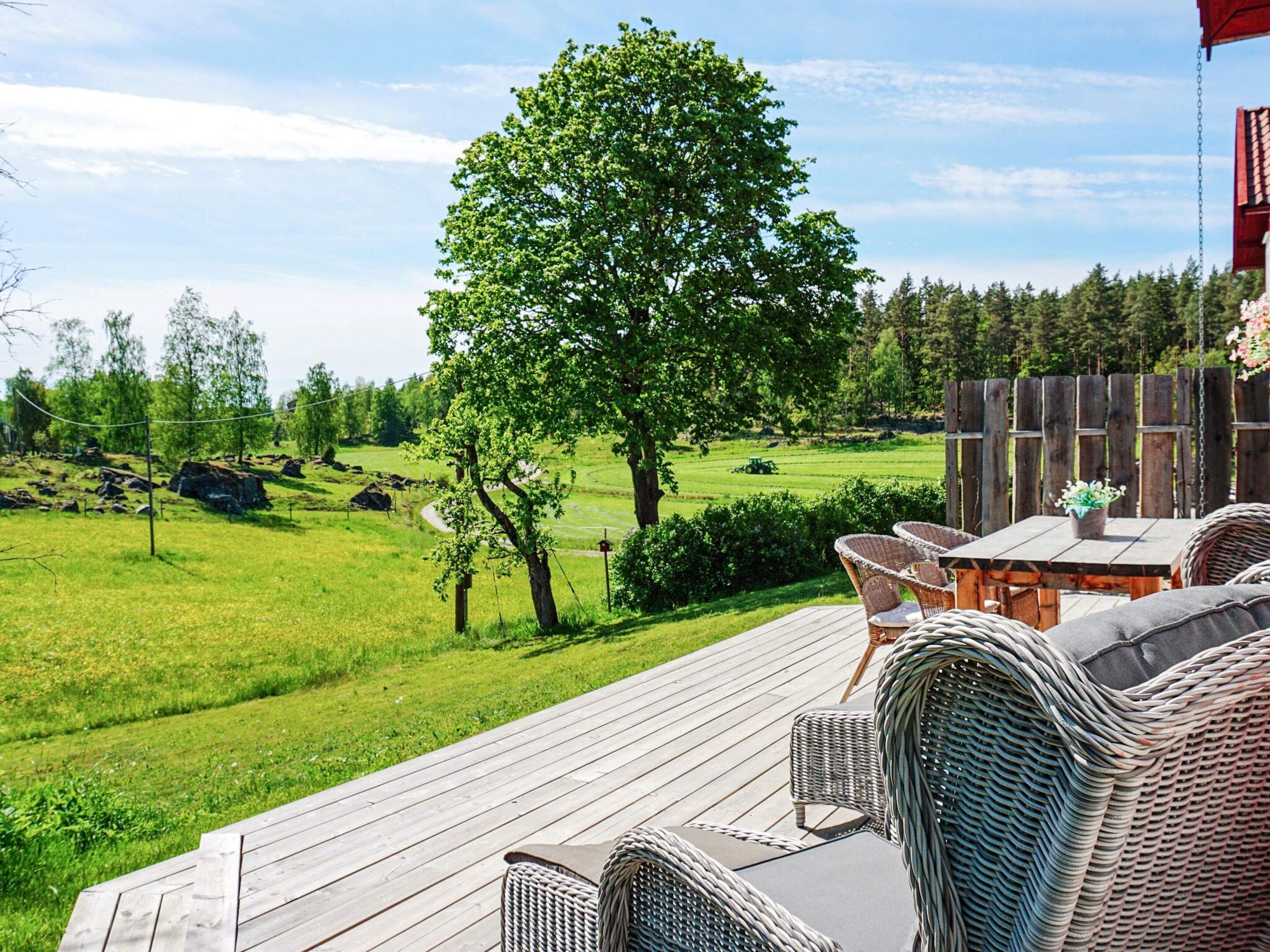 A deck with wicker furniture overlooking a grassy landscape with trees and a distant tractor.