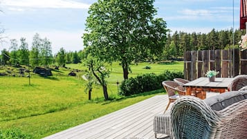 A deck with wicker furniture overlooking a grassy landscape with trees and a distant tractor.