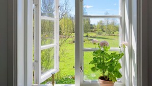 Ein offenes Fenster mit Blick auf eine grüne Landschaft und einem Blumentopf mit Blumen.