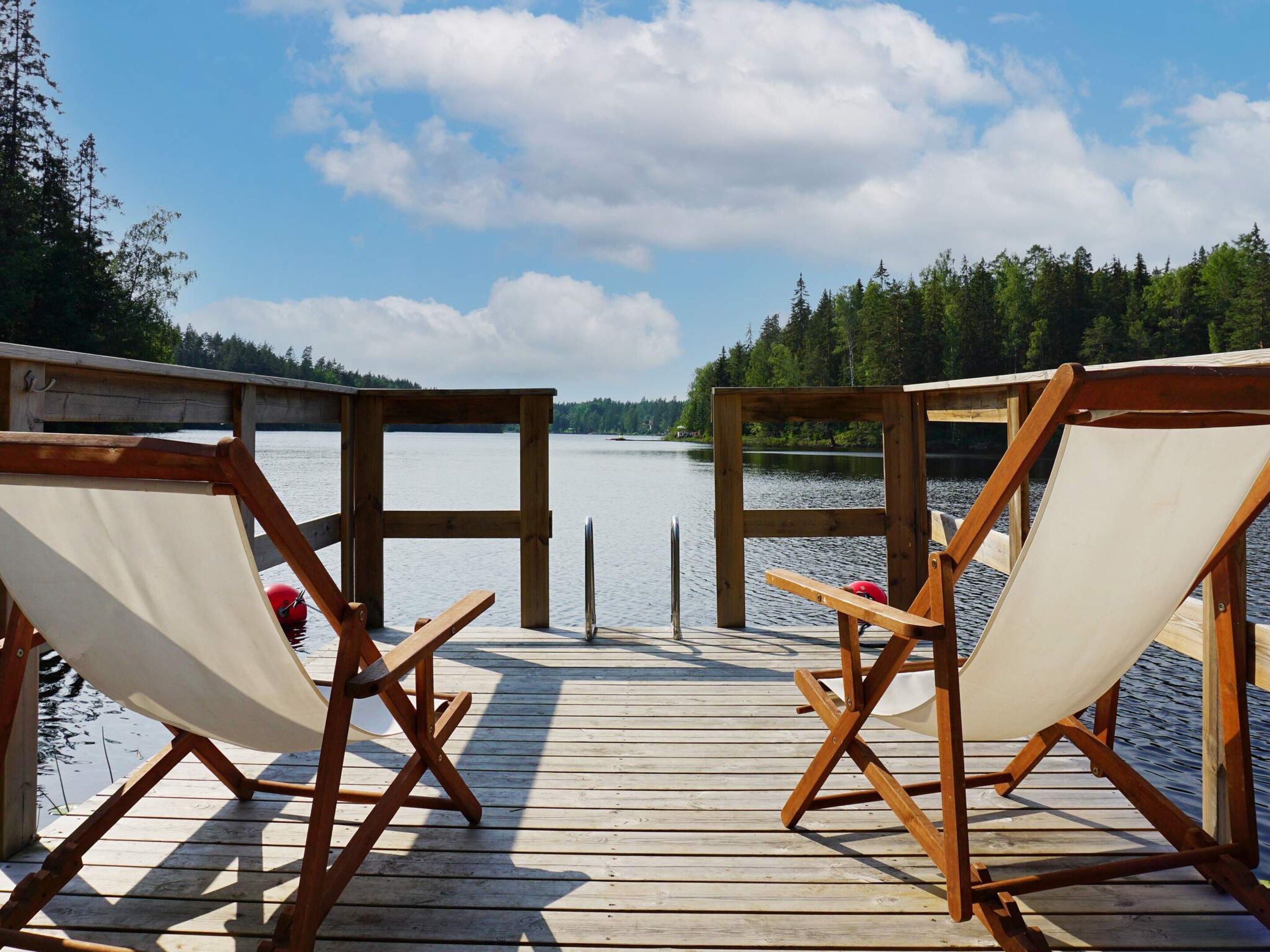 Een houten terras met twee canvas stoelen gericht op een kalm meer, omringd door bomen.