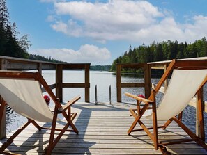 A wooden deck with two canvas chairs facing a calm lake, surrounded by trees and a clear sky. - 4 Person Holiday Home in Mellosa (Flen)