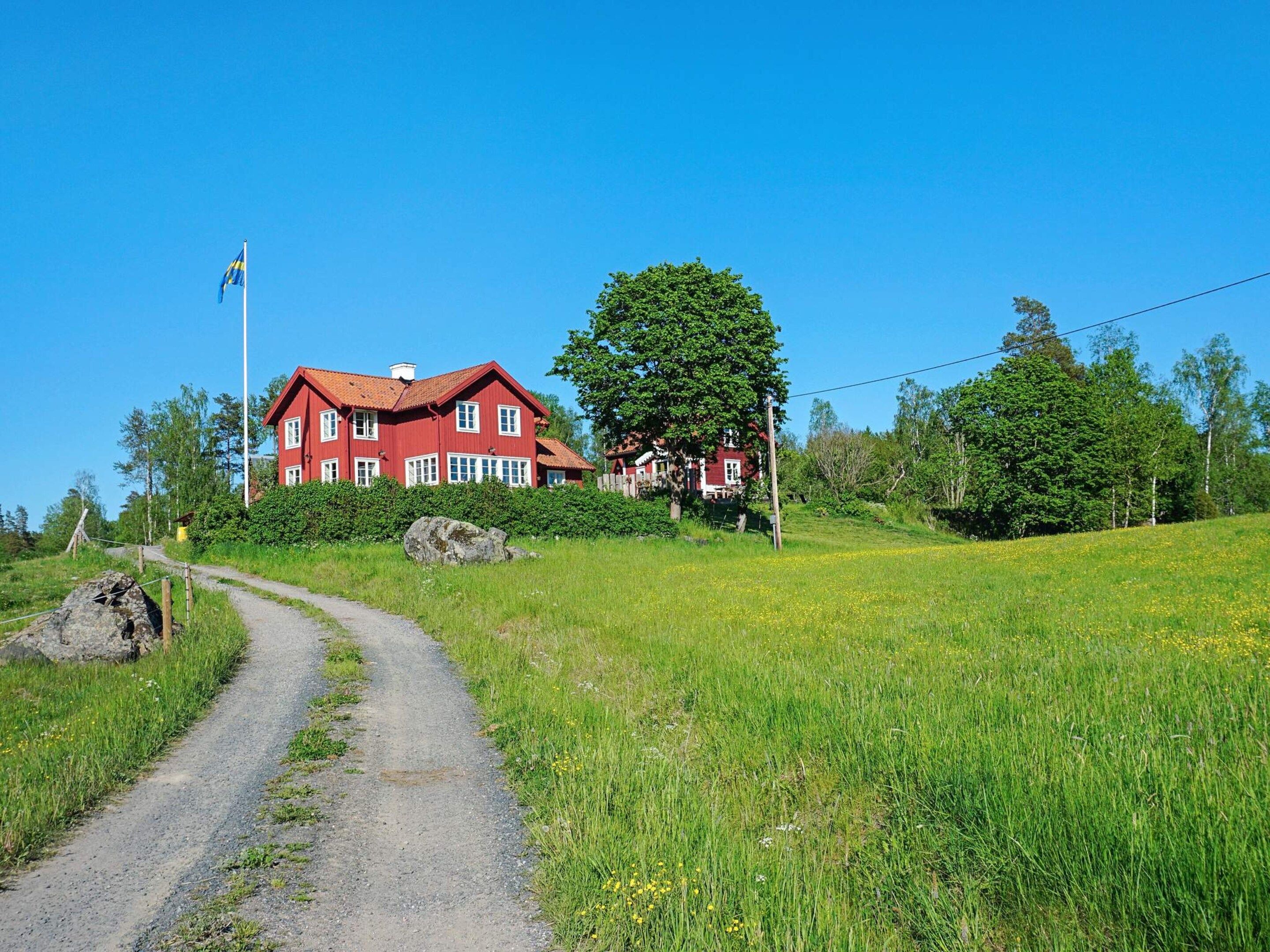 A red house with a flag, surrounded by greenery and a dirt path.