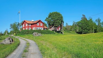 A red house with a flag, surrounded by greenery and a dirt path.