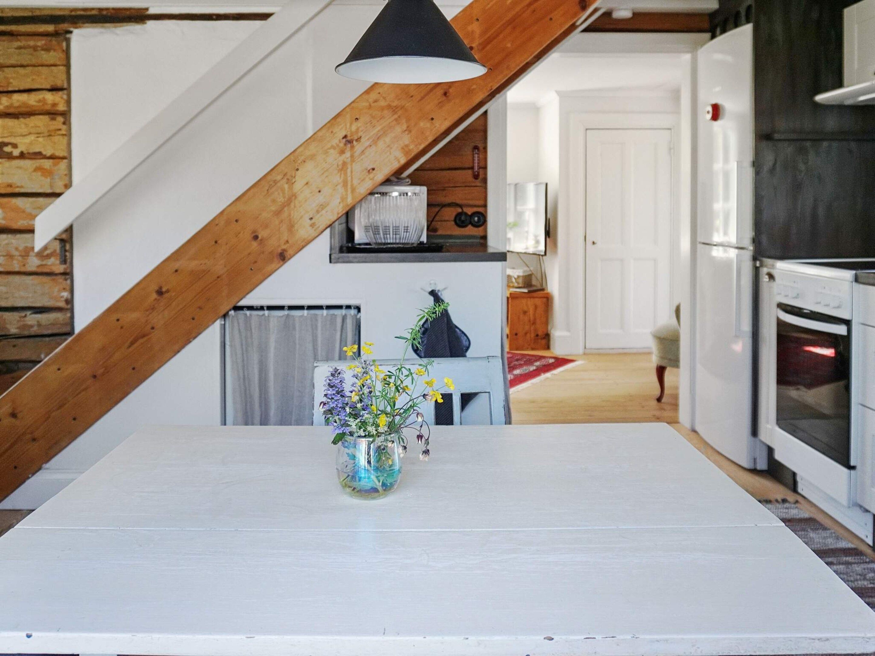 Une cuisine avec une table blanche, un vase de fleurs et un plafond en bois.