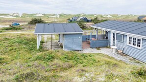 Ein Küstenhaus mit überdachter Terrasse, einer kleinen Außenterrasse und Blick auf die Dünen.