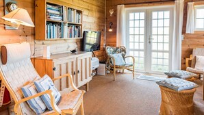 Ein gemütliches Blockhaus-Interieur mit Holzausbau, einer Bücherwand, einem Fernseher und bequemen Sitzmöglichkeiten.