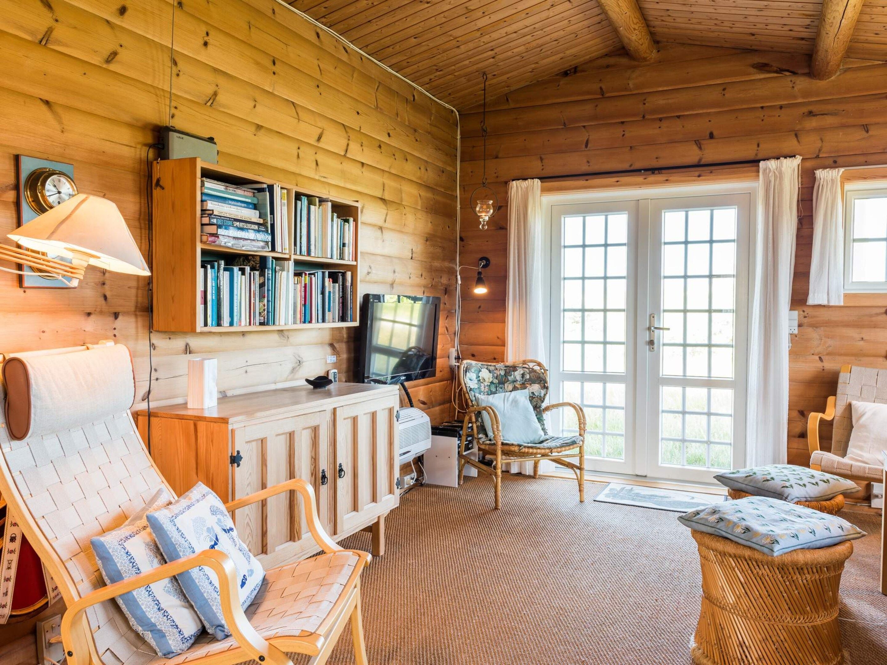 A cozy cabin interior with a wooden interior, a bookshelf, a television, and comfortable seating.