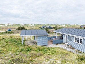 A coastal house with a covered patio, a small deck, and a view of the dunes.