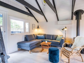 A room with a sectional sofa, a small wooden table, a blue ottoman, a wicker chair, and a black heater.