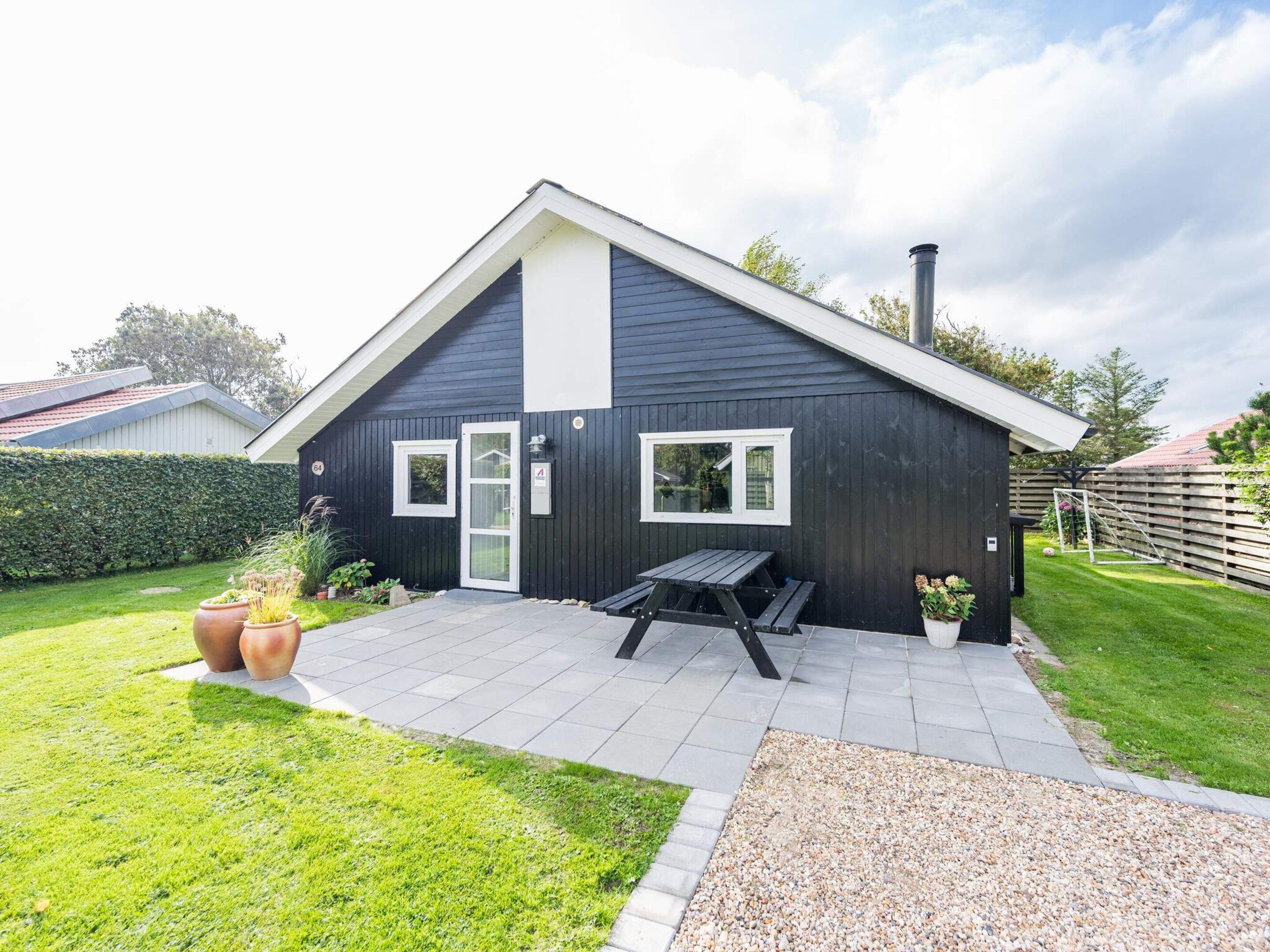 Une maison à deux étages, à l’extérieur sombre, avec une porte blanche et un petit patio comprenant une table et des chaises.