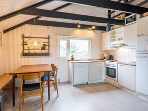 A modern kitchen with white cabinetry, a wooden dining table, and a hanging light fixture. - 4 Star Holiday Home in Hemmet (Hemmet)