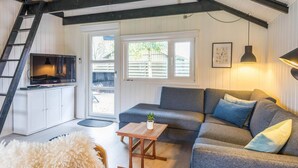 Un espace de vie de style loft avec un canapé d’angle gris, une table basse en bois, un téléviseur posé sur un meuble blanc et une échelle.