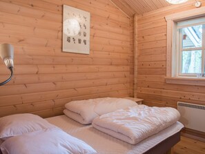 Una habitación de cabaña de madera con una cama, una lámpara de pared y un ventanal.