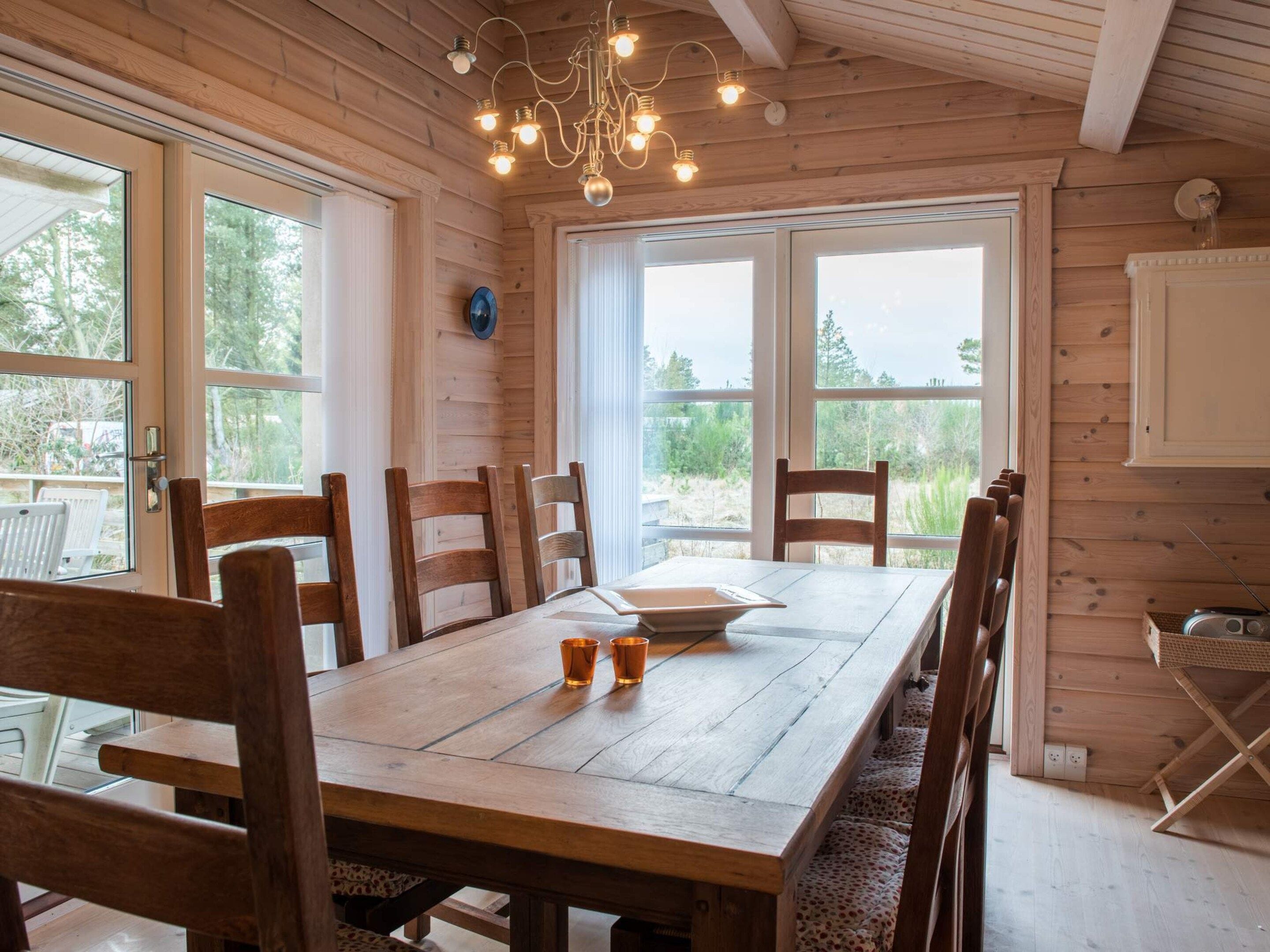 Ein Holzinnenraum mit Esstisch, Stühlen und einer Chandelüster.