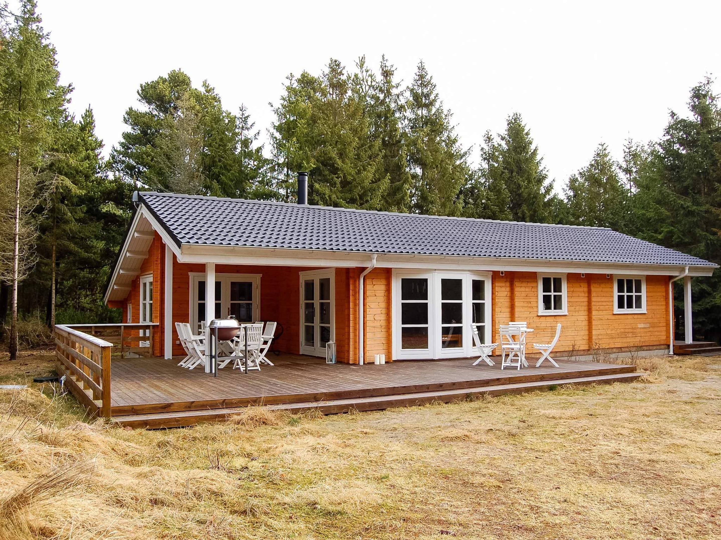 A wooden cabin with a tiled roof, large windows, and a deck with outdoor furniture.