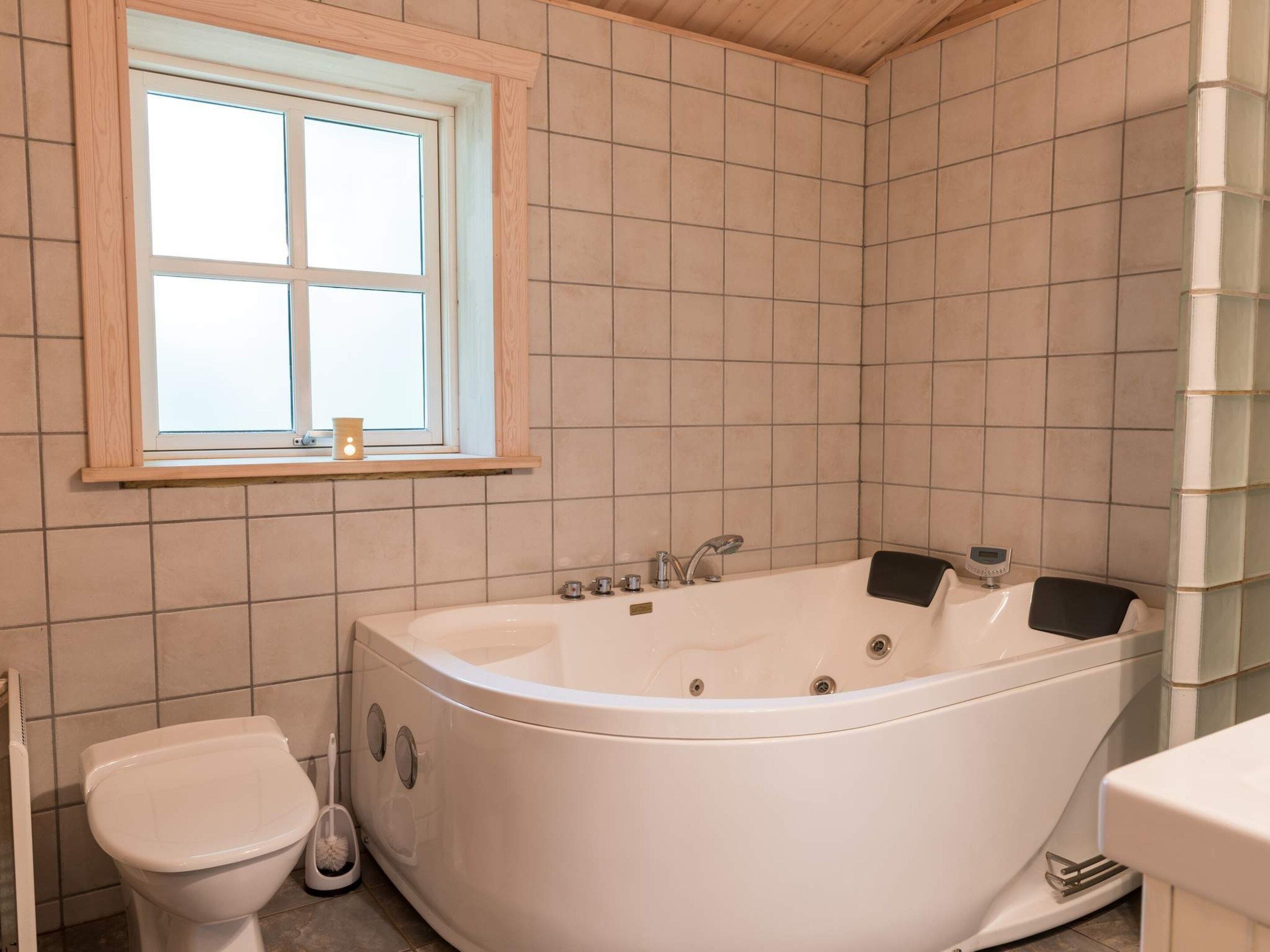 A bathroom with a bathtub, toilet, and window.