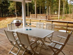 A wooden deck with a table and chairs, a grill, and a stack of firewood. - 4 Star Holiday Home in Norre Nebel (Norre Nebel)