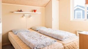 A small, cozy room with two beds, a shelf with decorative items, and a window. - Tranquil Cottage With Spa and Sauna-by Traum (Hemmet)