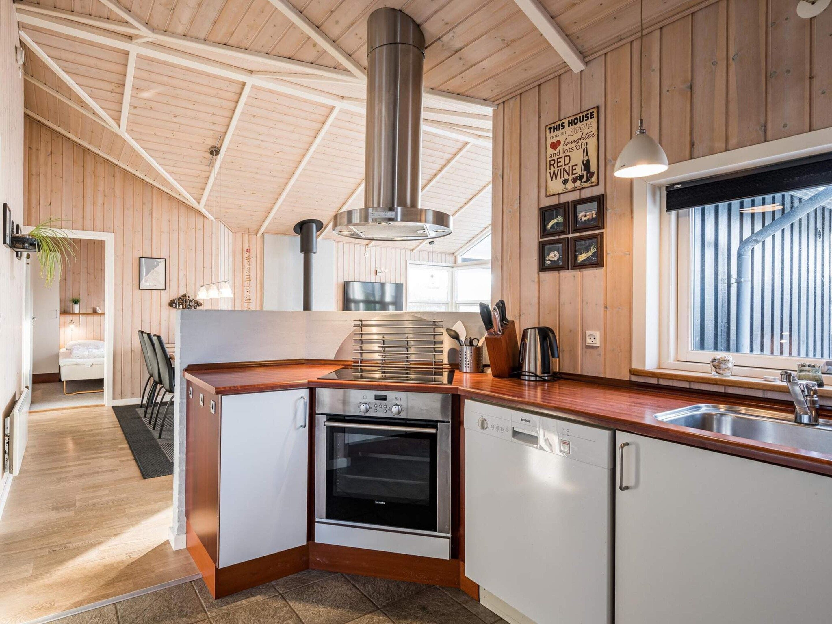 Een kleine keuken met houten wanden, een roestvrijstalen afzuigkap en een Bosch vaatwasser.